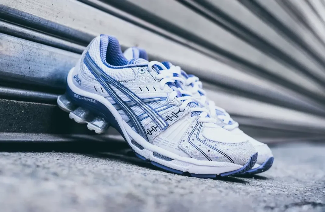 Tenis ASICS GEL-Kinsei en tonos blancos y azules sobre fondo urbano metálico con estética retro-running